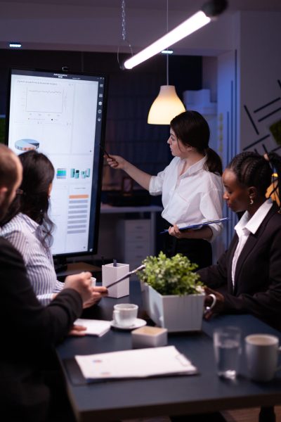 Executive manager woman explaining management statistics working at company strategy overtime in office meeting room. Diverse multi-ethnic businesspeople teamwork brainstorming ideas in evening.