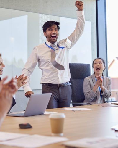 Multi-Cultural Business Team Celebrating Deal Around Table In Modern Office Building