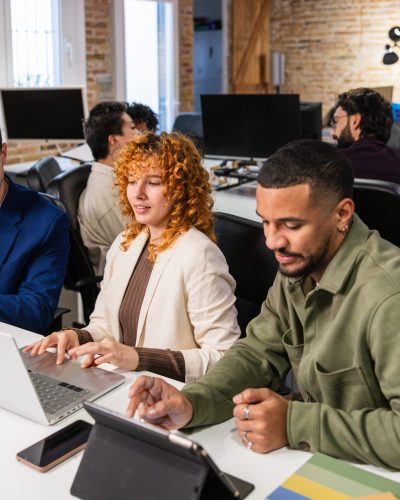 Coworkers collaborating with laptops and tablets, engaged in discussions and brainstorming sessions in a bright, modern office environment