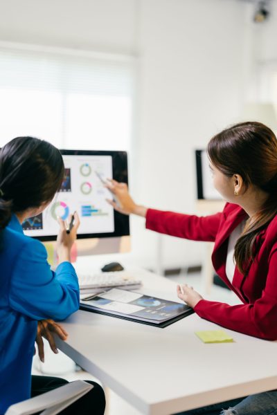 Two businesswomen discussing financial data on a computer, strategizing for the future with teamwork and collaboration